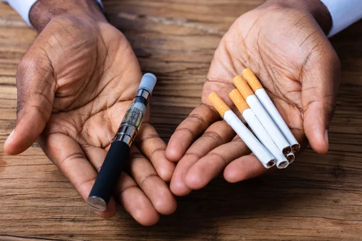 hands-holding-a-vape-pen-and-cigarettes-dh-vape